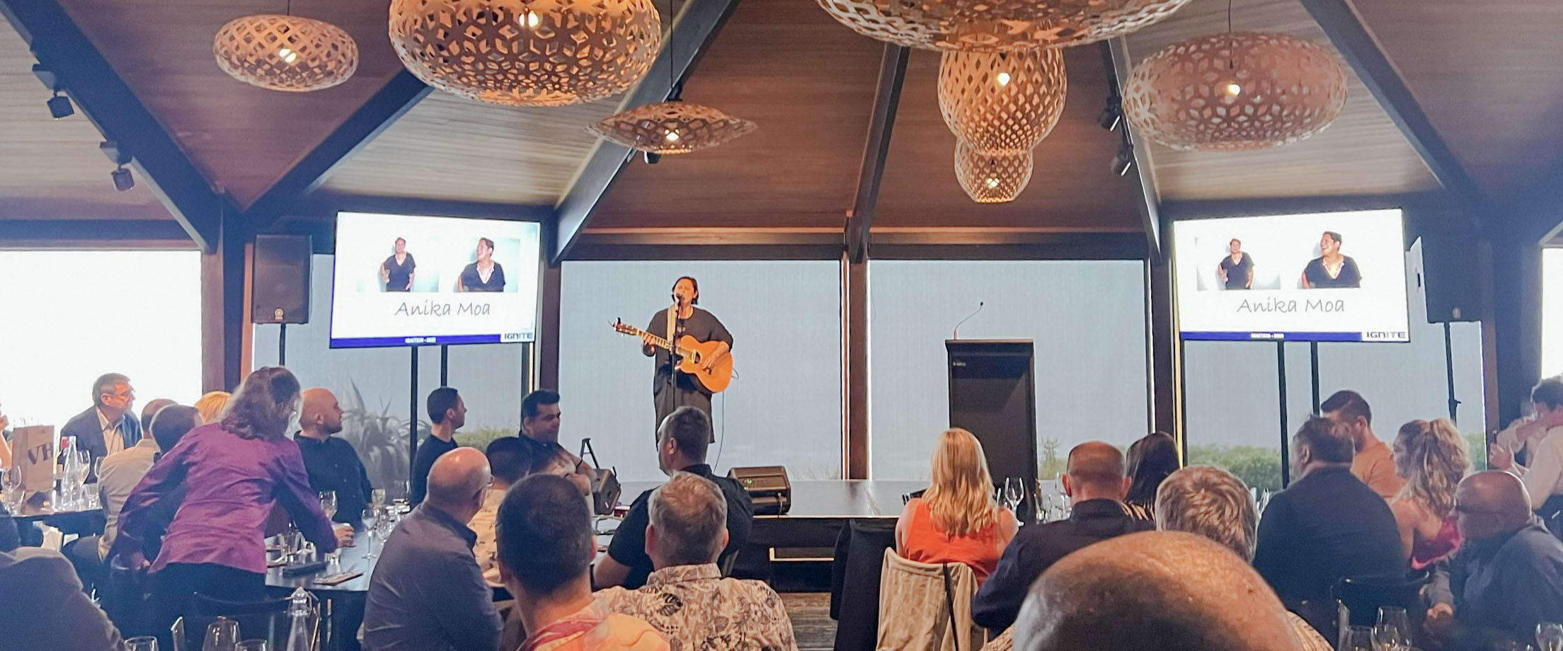 Live performer framed by two presentation screens at a dinner event